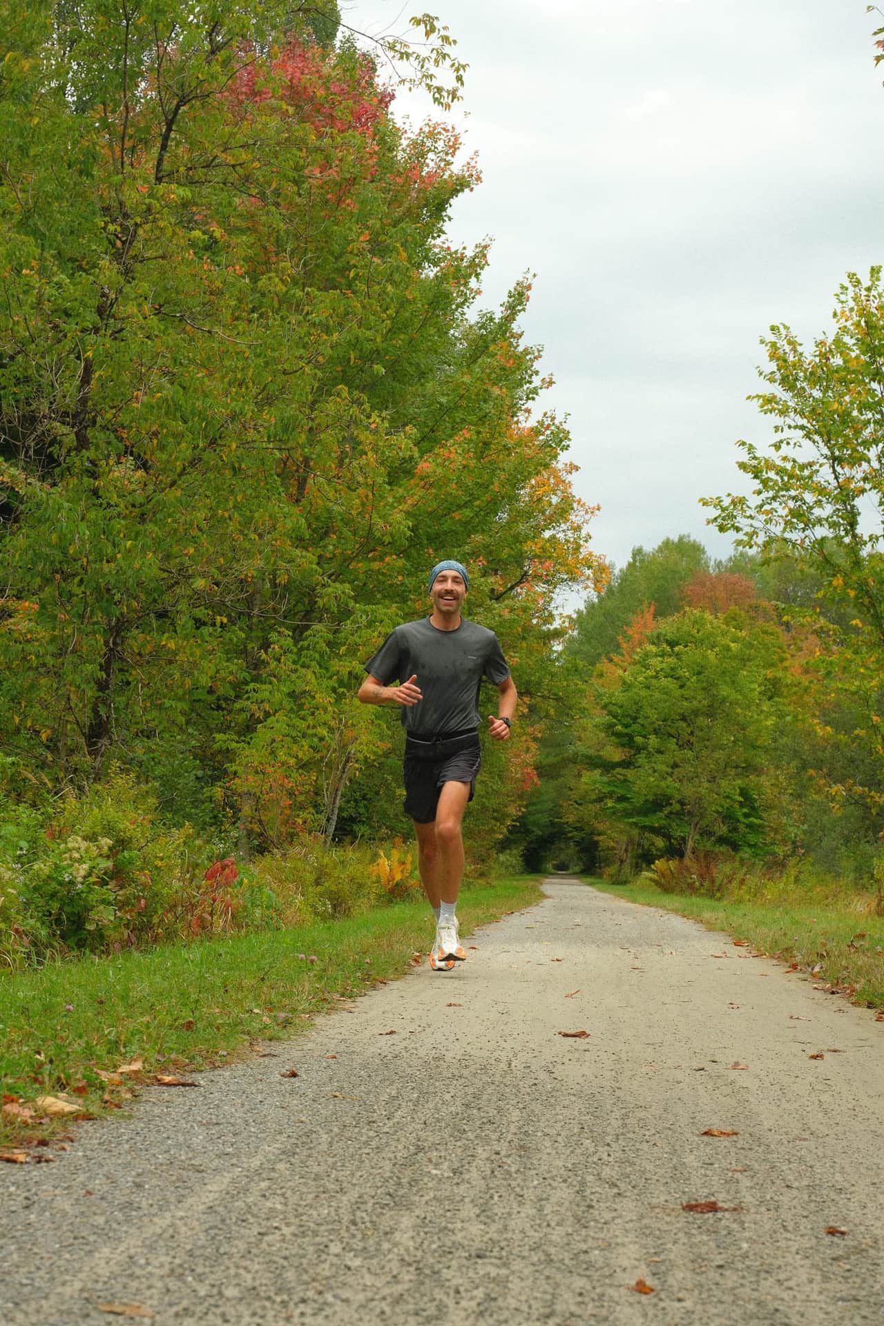 Un coureur sur le large sentier de poussière de pierre, entre les arbres aux couleurs d'automne.