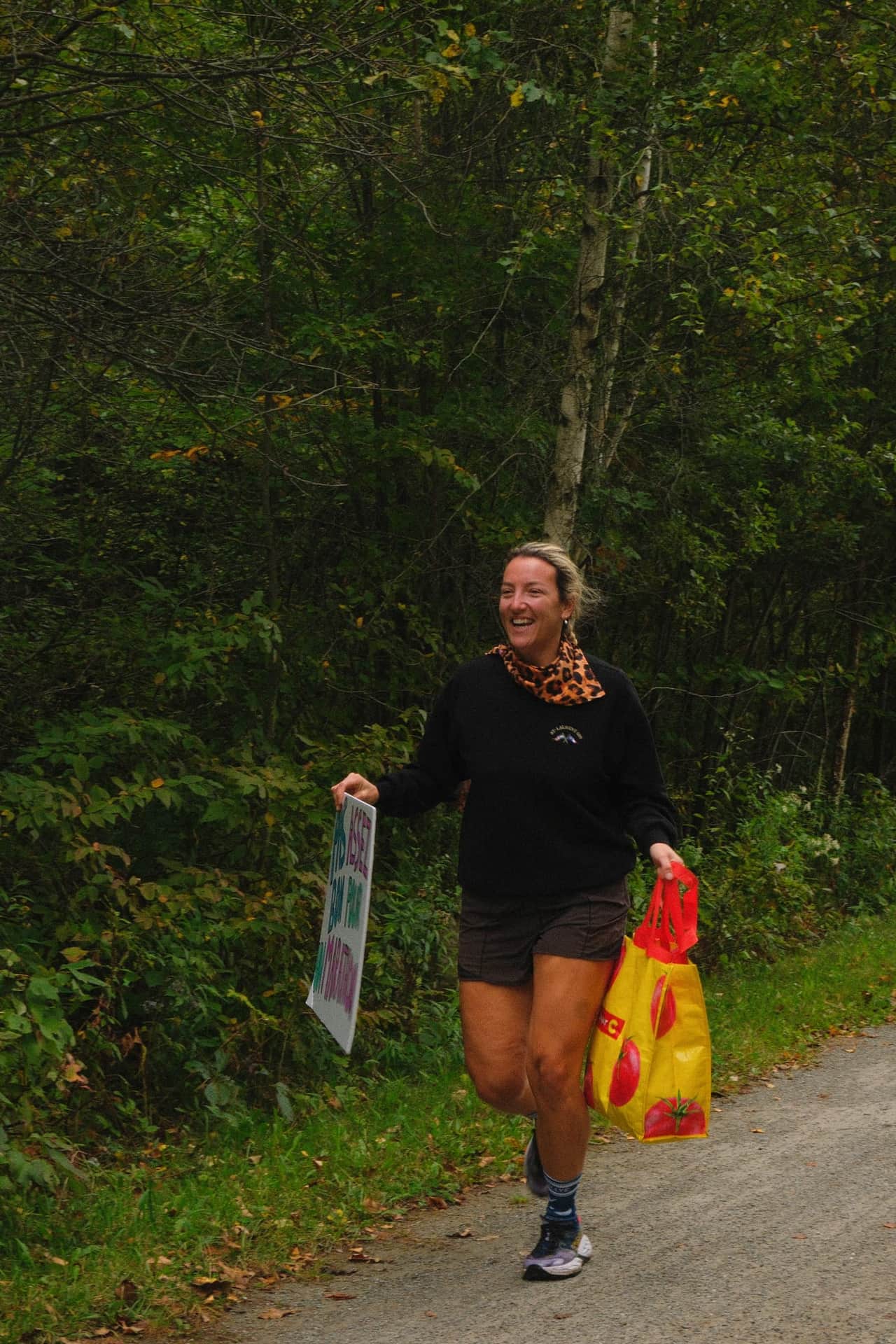 Une spectatrice souriante encourage les coureurs au bord du sentier, une pancarte à la main.