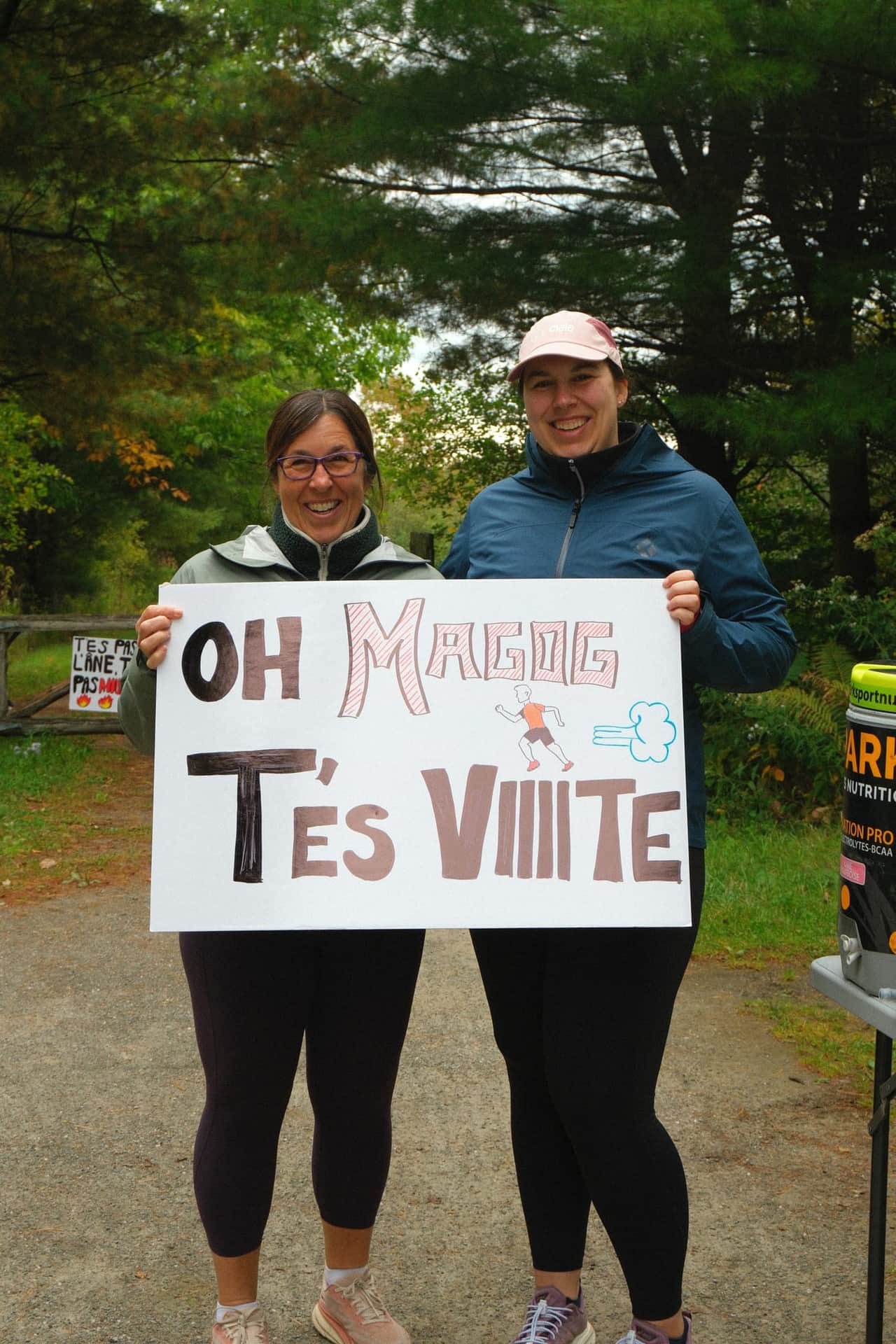 Deux spectatrices tiennent une pancarte « Oh Magog, t'es viiite » au bord du sentier.